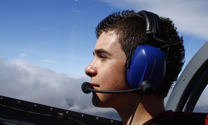 A trial-flight student at the controls, headset on, flying over the Cotswolds